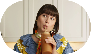 A woman drinking a smoothy in her kitchen while deep in thought.